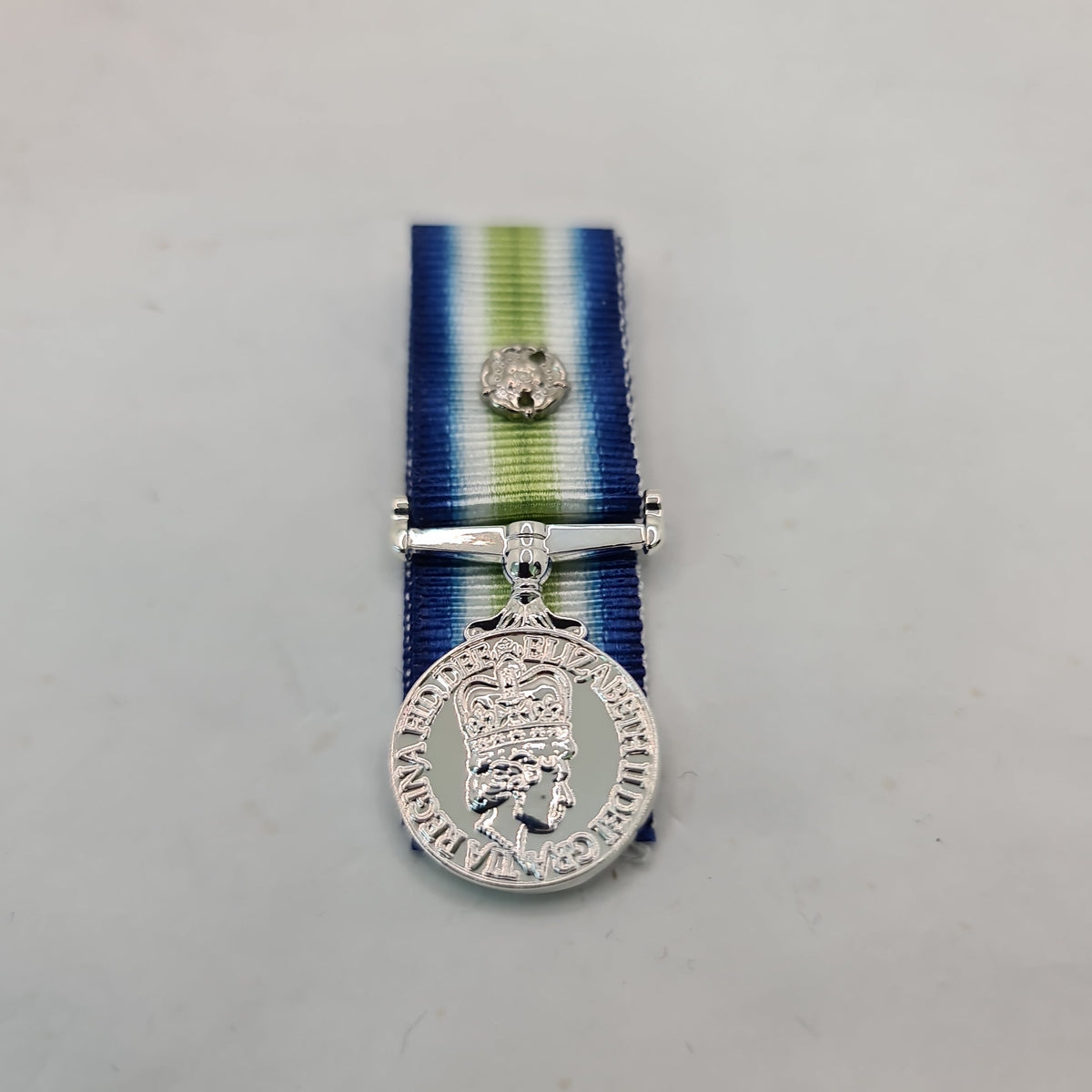 A silver-toned military medal with a blue, white, and green striped ribbon, suspended from a silver bar, photographed against a plain light gray background.