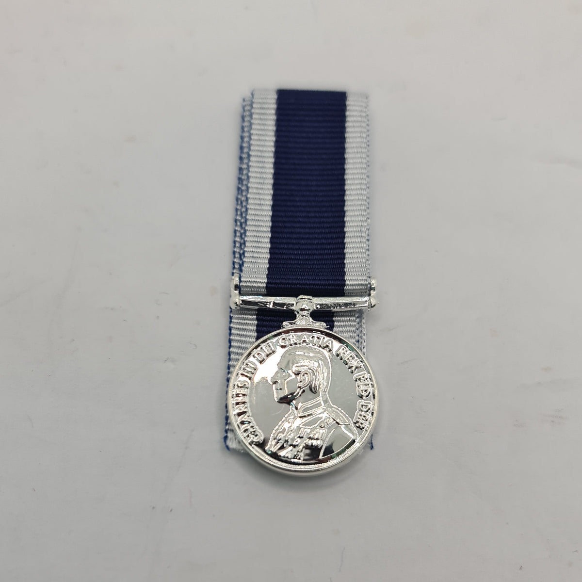 Navy miniature medal with a profile portrait of a king, attached to a blue ribbon, against a white background.