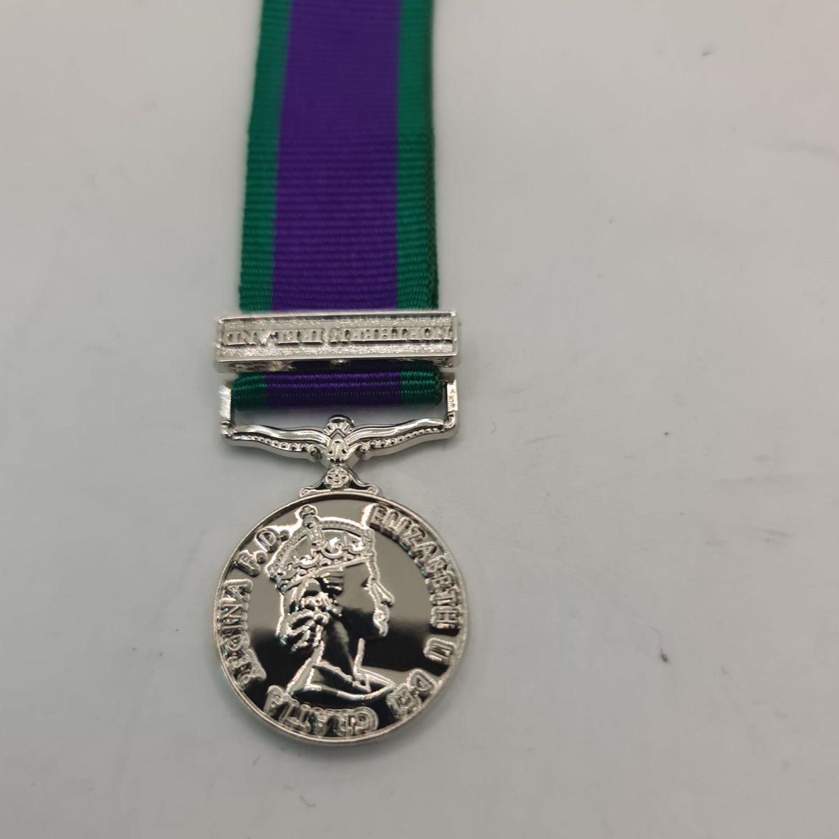 A miniature GSM NI award medal with a green ribbon, displayed against a white background.